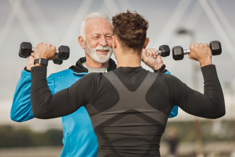 Personal trainer acompanhando o treino de um aluno com halteres