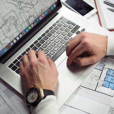 Mãos no teclado de um notebook ao lado de plantas impressas