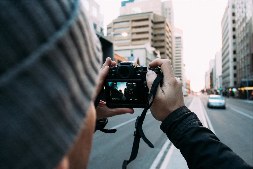 Câmera fotográfica nas mãos de quem fotografa, numa rua da cidade
