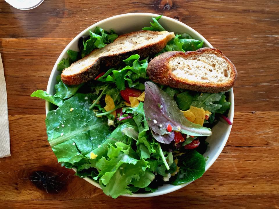 Salada colorida com pão em uma mesa de madeira