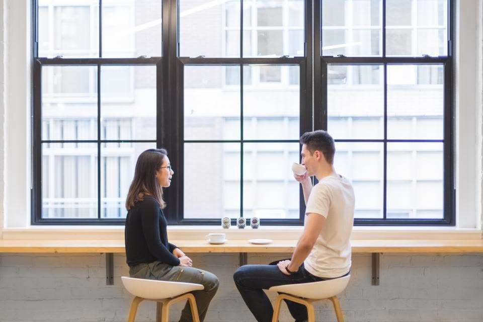 Duas pessoas conversando sentadas perto de uma janela ampla